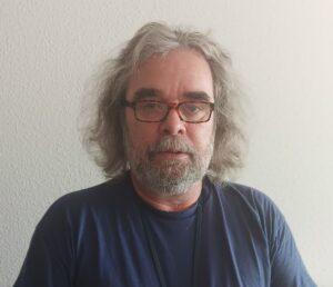 Bild von Thomas Künnecke. Er hat graue Haare, einen Bart und trägt ein dunkelblaues Oberteil.